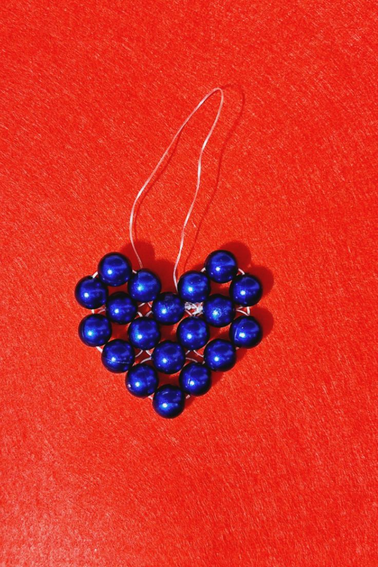 blue beads are arranged in the shape of a heart on a red surface with white thread