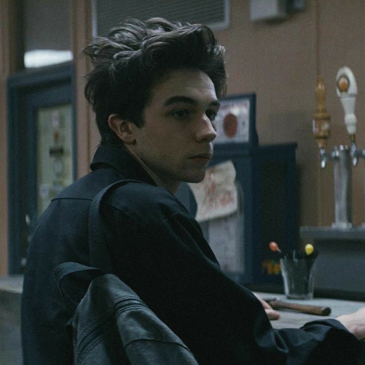 a young man sitting at a table with food in front of him and looking off into the distance