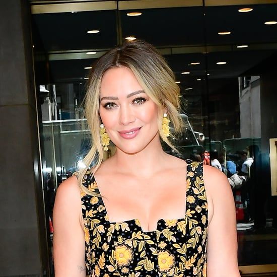 a woman with blonde hair wearing a black and yellow floral dress standing in front of a glass door