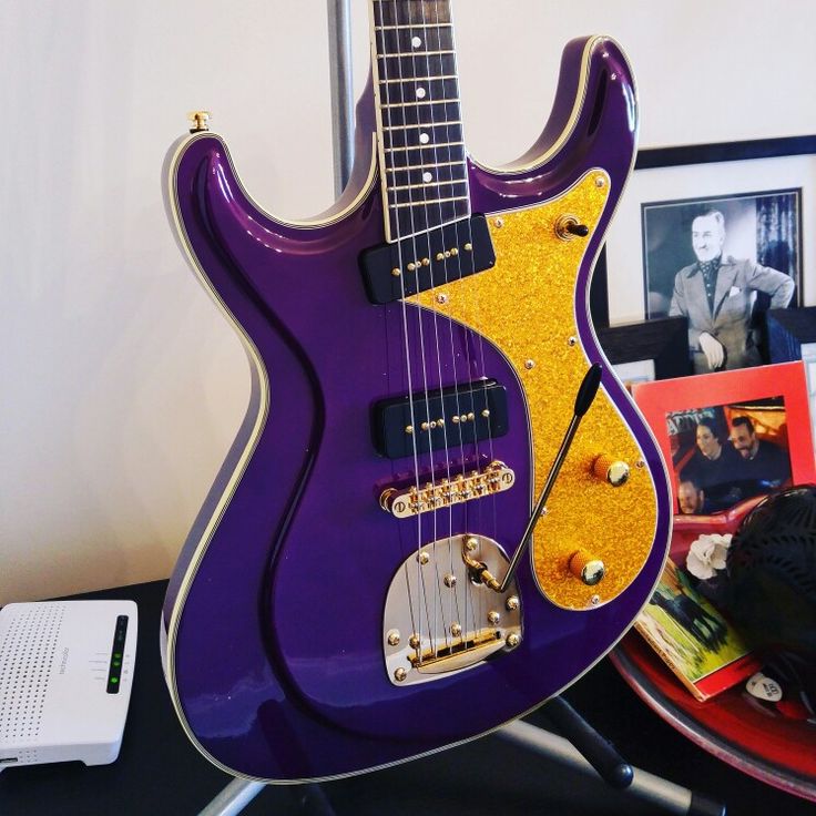 a purple and yellow guitar sitting on top of a table next to a laptop computer