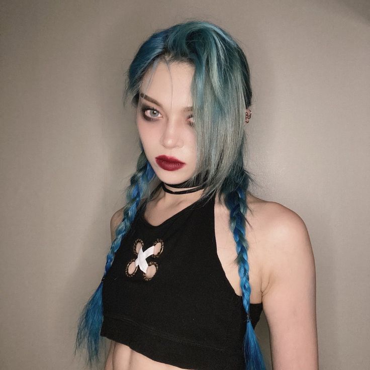 a woman with blue hair wearing a black crop top and red lipstick is standing in front of a wall