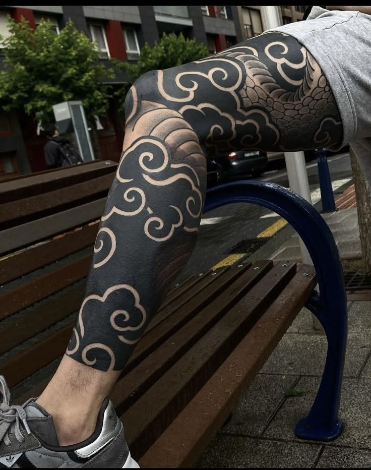 a man is sitting on a bench with his leg covered in black and white tattoos