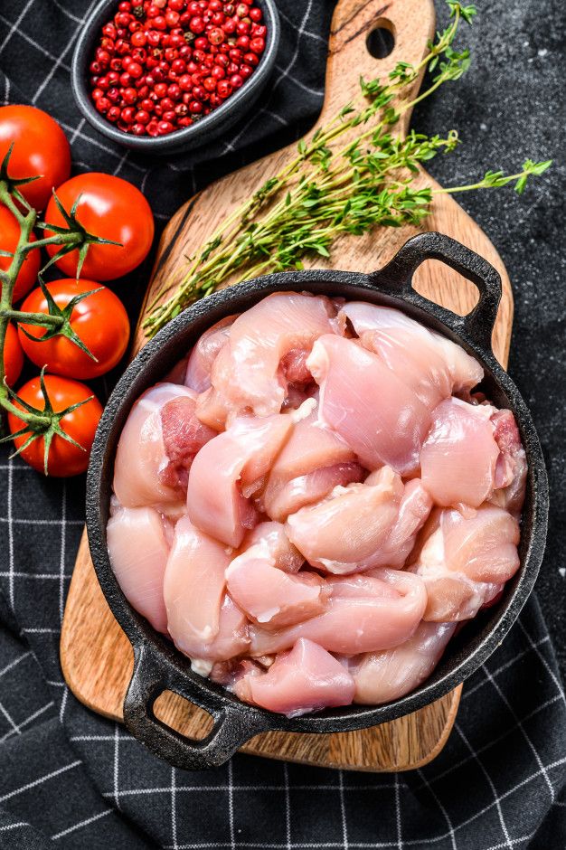 raw chicken in a cast iron skillet with tomatoes, herbs and seasoning on the side