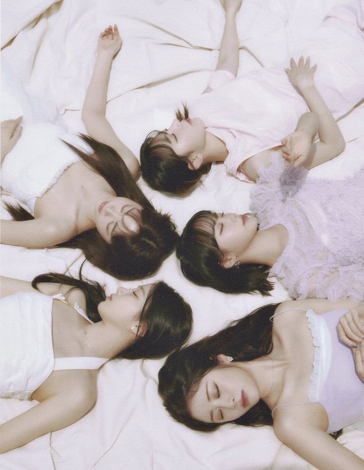 four young women laying on top of a bed next to each other with their hands in the air