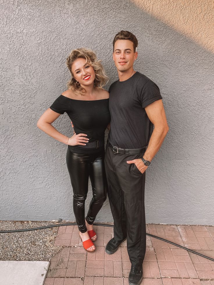 a man and woman standing next to each other in front of a gray wall wearing black leather pants