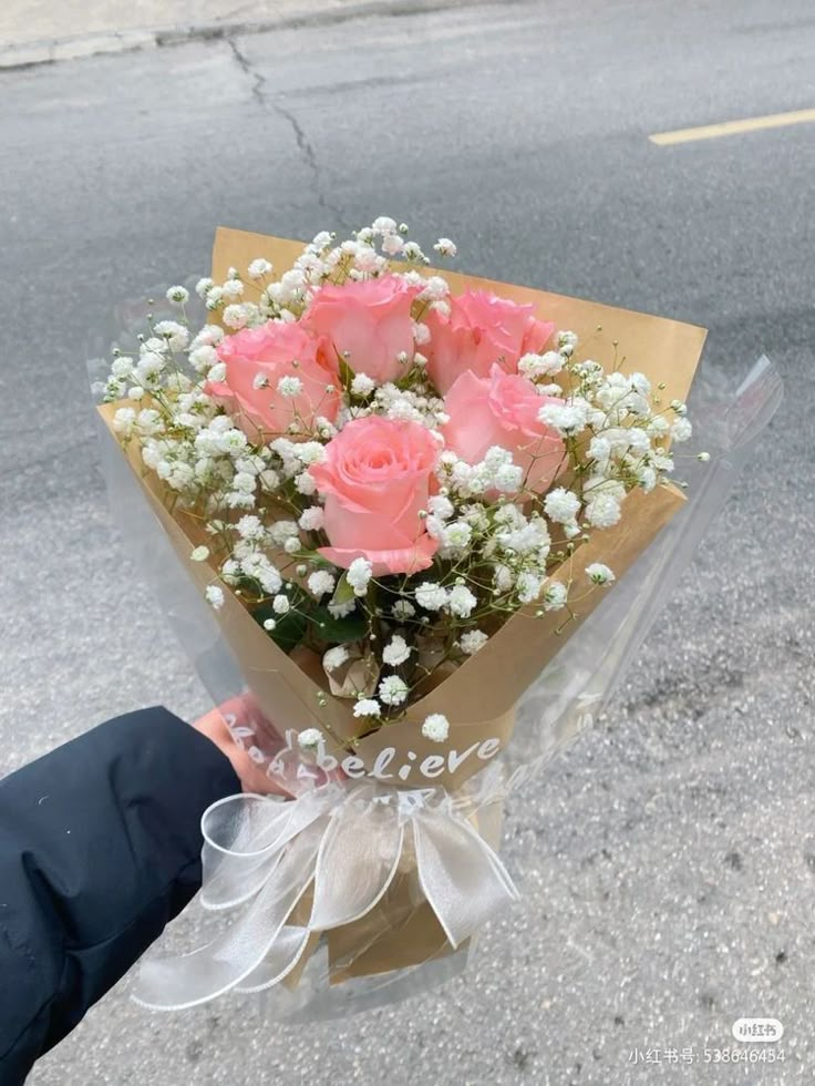 someone holding a bouquet of pink roses on the street