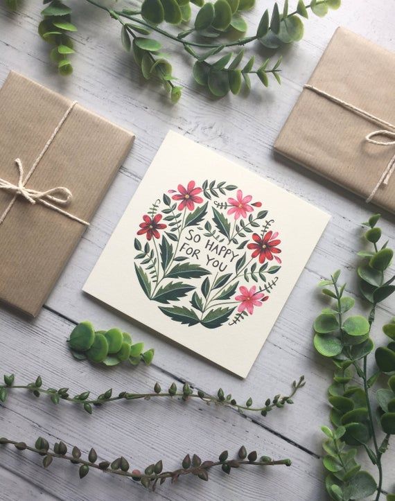 a card with some flowers on it next to two wrapped gifts and greenery leaves