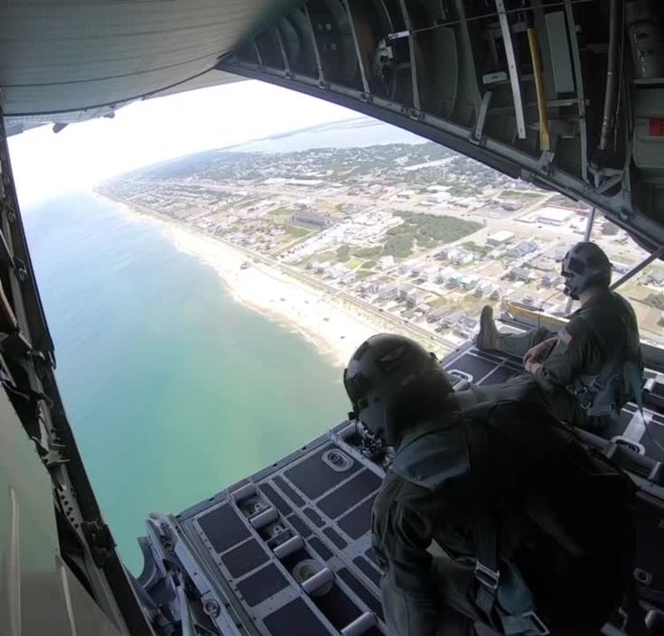 two men are sitting in the cockpit of an airplane looking out at the water and land