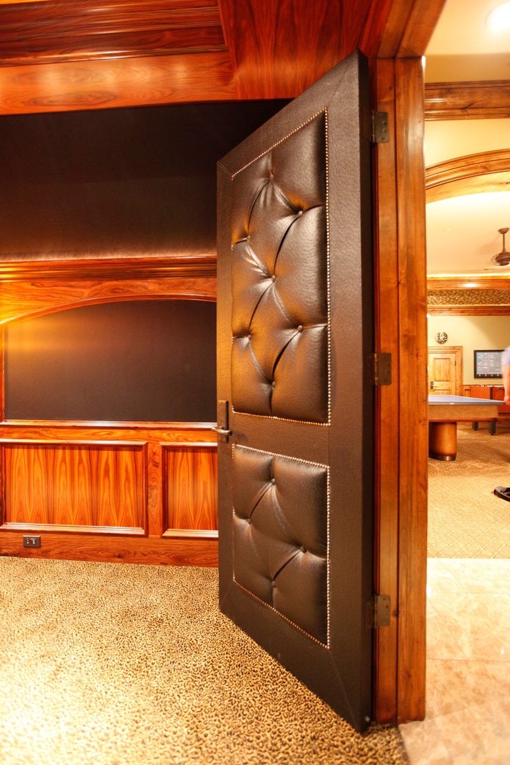 an open door in the middle of a room with wood paneling and leather upholstered panels