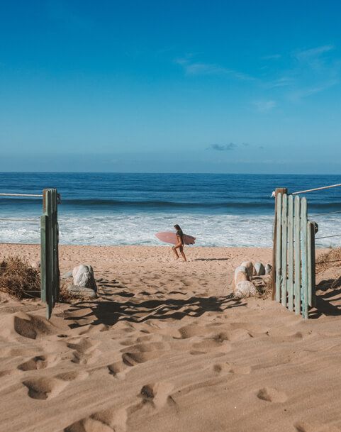 a person carrying a surfboard on top of a sandy beach next to the ocean