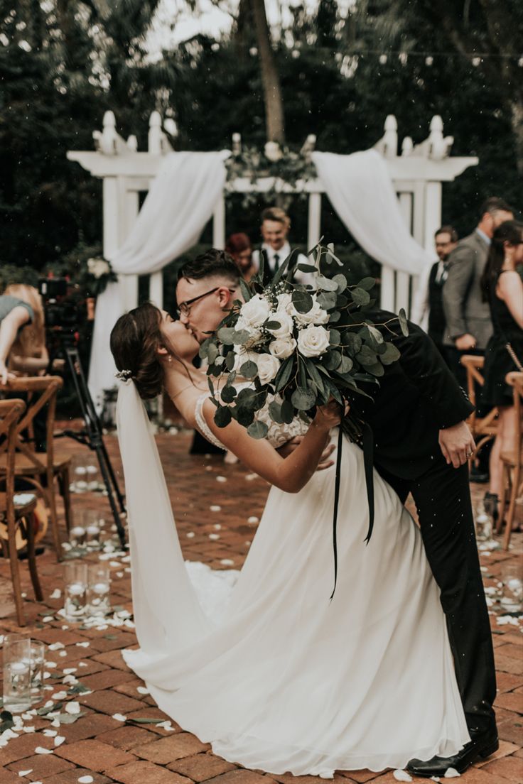 a bride and groom kissing in front of an outdoor wedding ceremony with white flowers on the ground