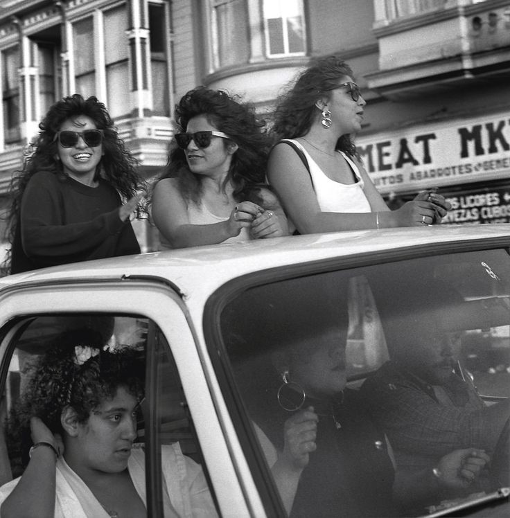 black and white photograph of three women sitting in the back of a car on a city street