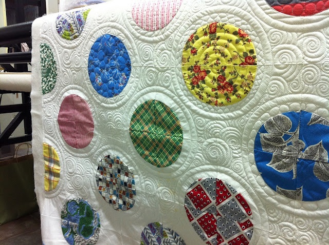 a white quilt with many different colored circles on the front and back, hanging from a black ironing rod