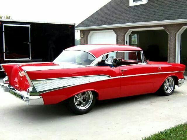 an old red car parked in front of a garage