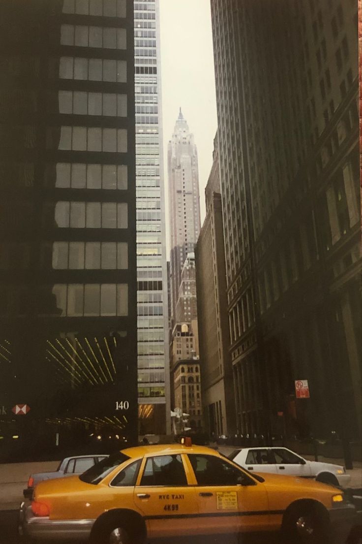 a yellow taxi cab driving down a street next to tall buildings in new york city