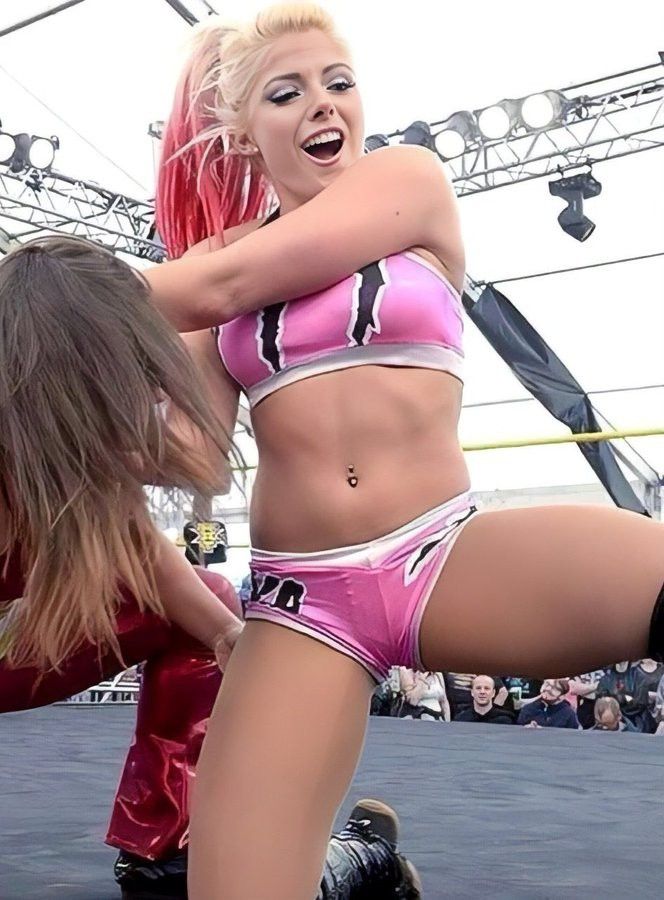 two women on roller skates in front of an audience at a sporting event, one wearing pink and the other black