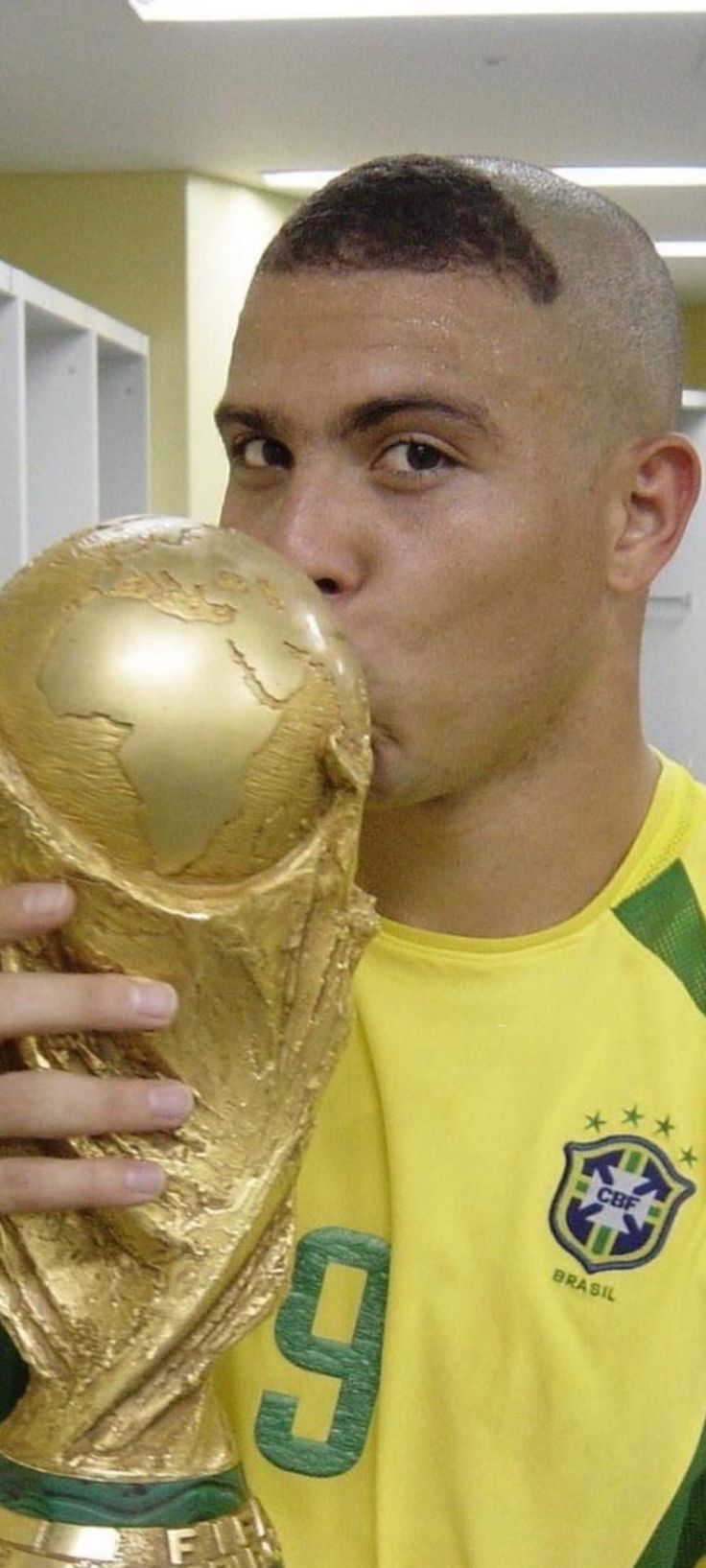 a man in a yellow shirt kissing a golden ballon d'or winner trophy