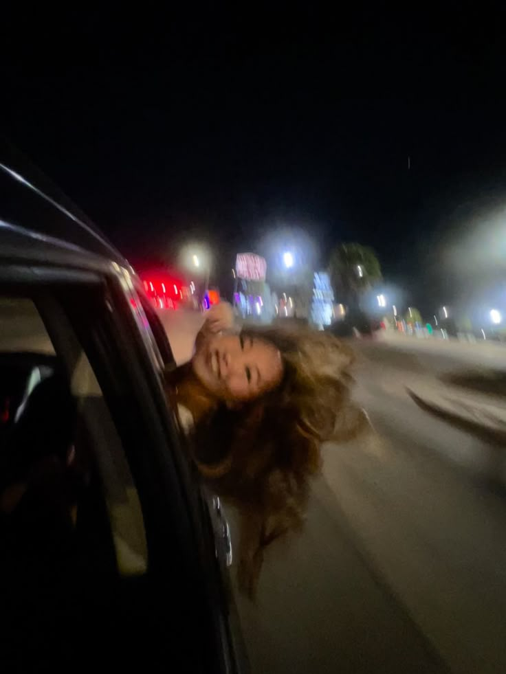 a woman leaning out the window of a car at night