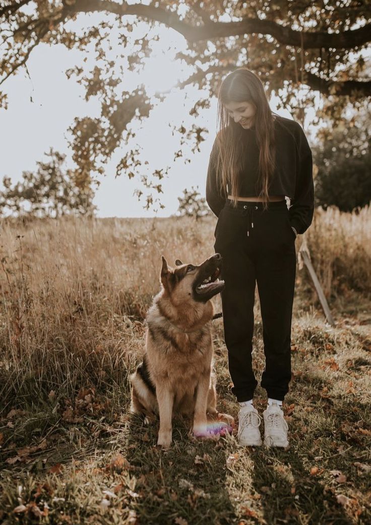 a woman standing next to a dog in a field