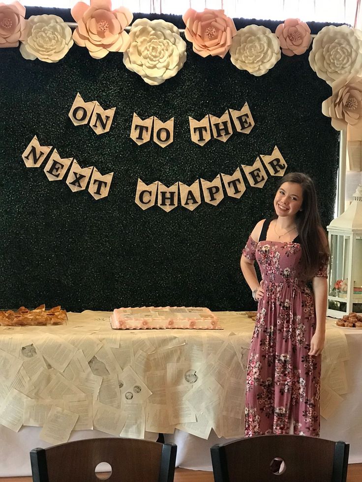 a woman standing in front of a table with cake on it and flowers hanging from the wall