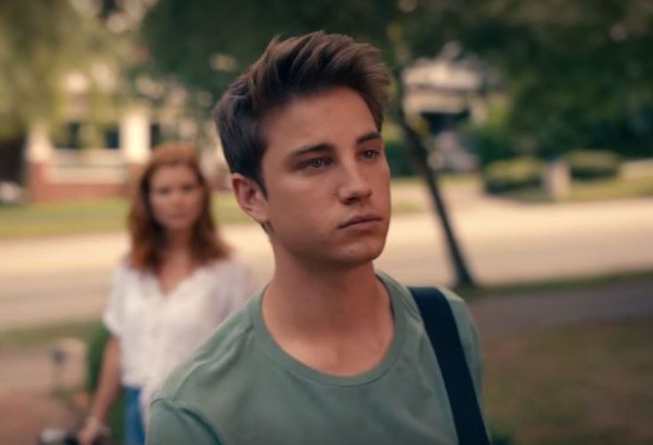 two people walking down the street with trees in the background and one person looking at the camera