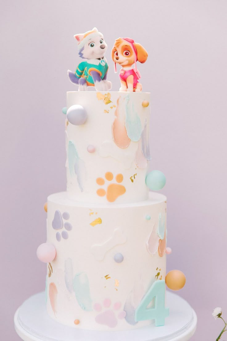 there is a white cake with paw patrol decorations on the top and two small figurines atop it