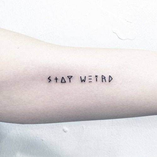 a person's arm with the words stay weird tattooed in black ink on it