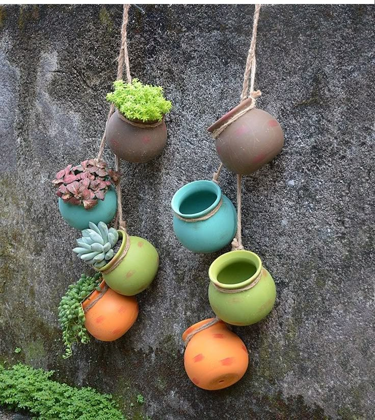 four hanging pots with plants and succulents attached to them on a rock