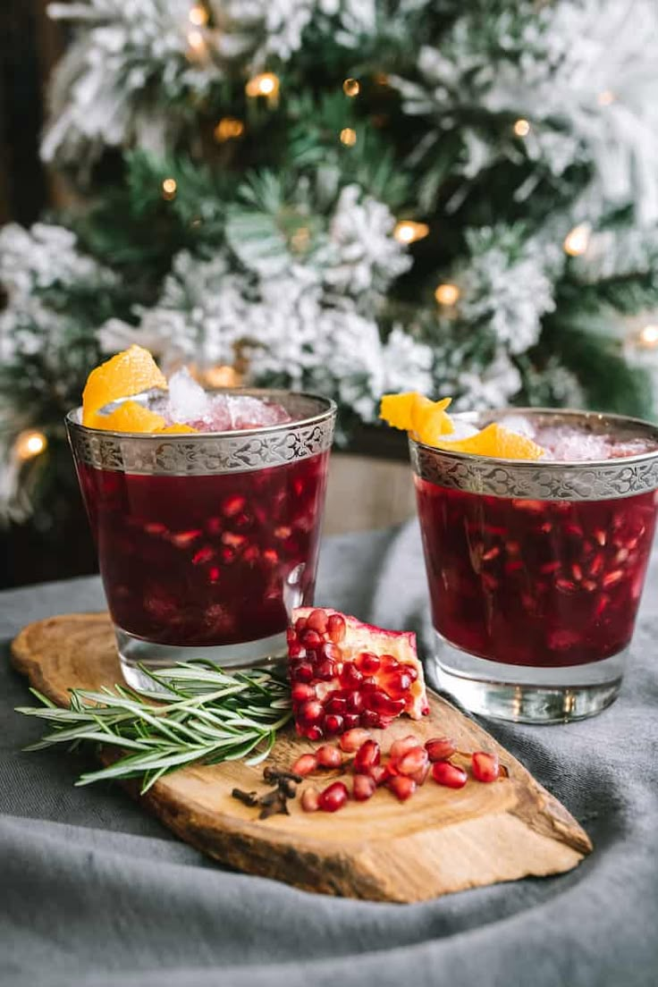 two glasses filled with pomegranate on top of a wooden cutting board next to a christmas tree