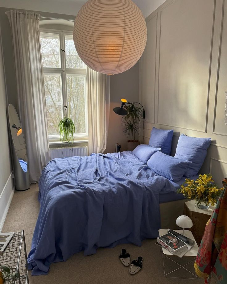 a bed with blue sheets and pillows next to a window in a room filled with plants