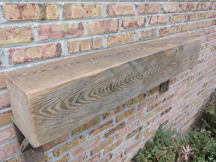 a wooden shelf on the side of a brick wall next to green bushes and shrubbery