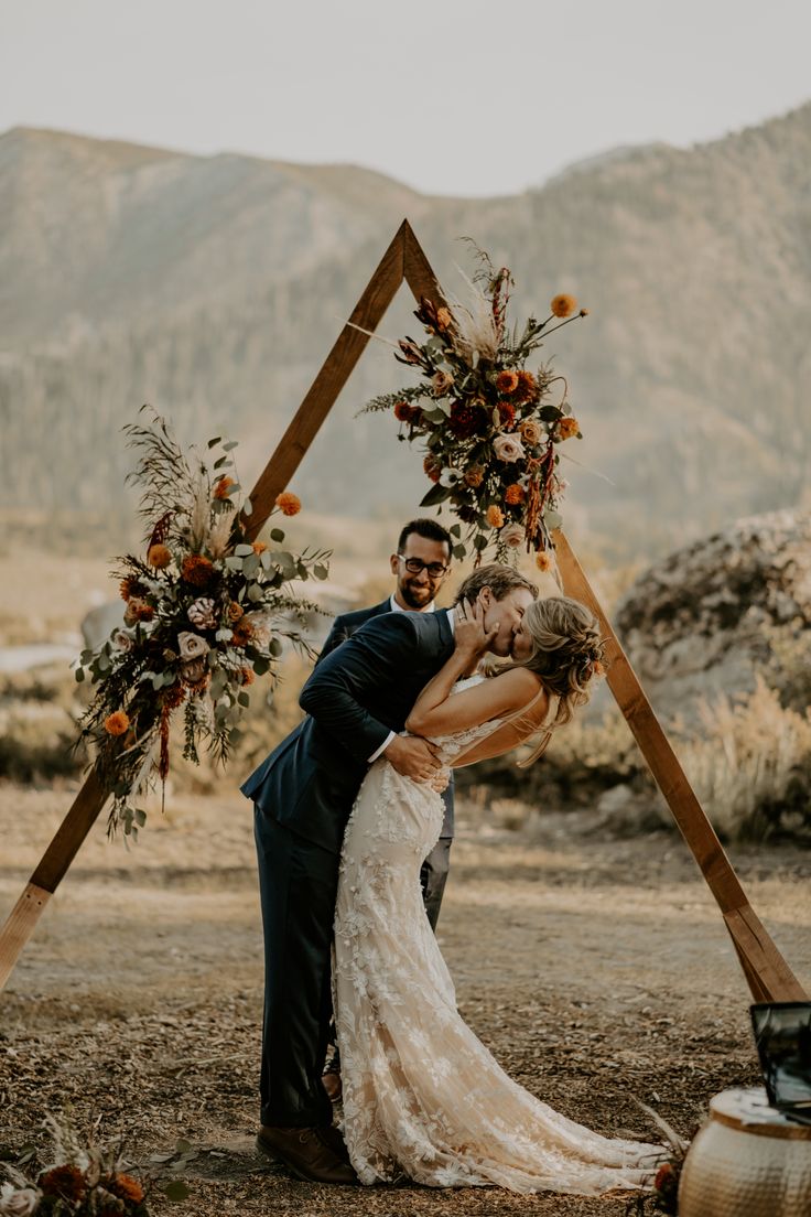 a bride and groom kissing in front of an arch made out of wood sticks with flowers