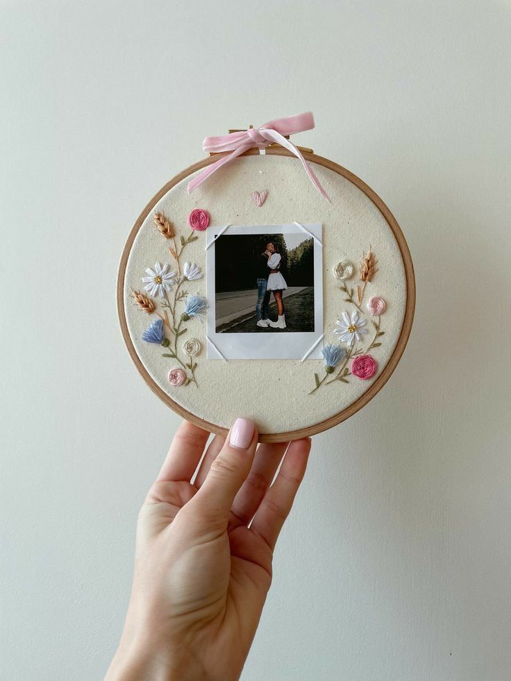 a person holding up a small embroidery frame with a photo on it and pink ribbon around the edge