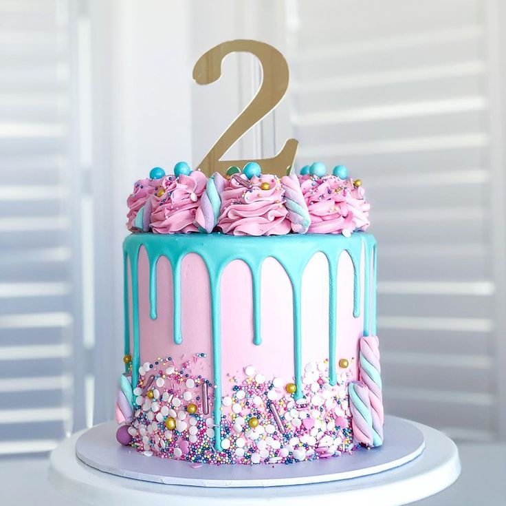 a birthday cake with pink and blue icing, sprinkles and a number two on top