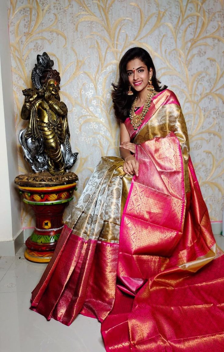 a woman in a pink and gold sari posing for the camera with her hands on her hips