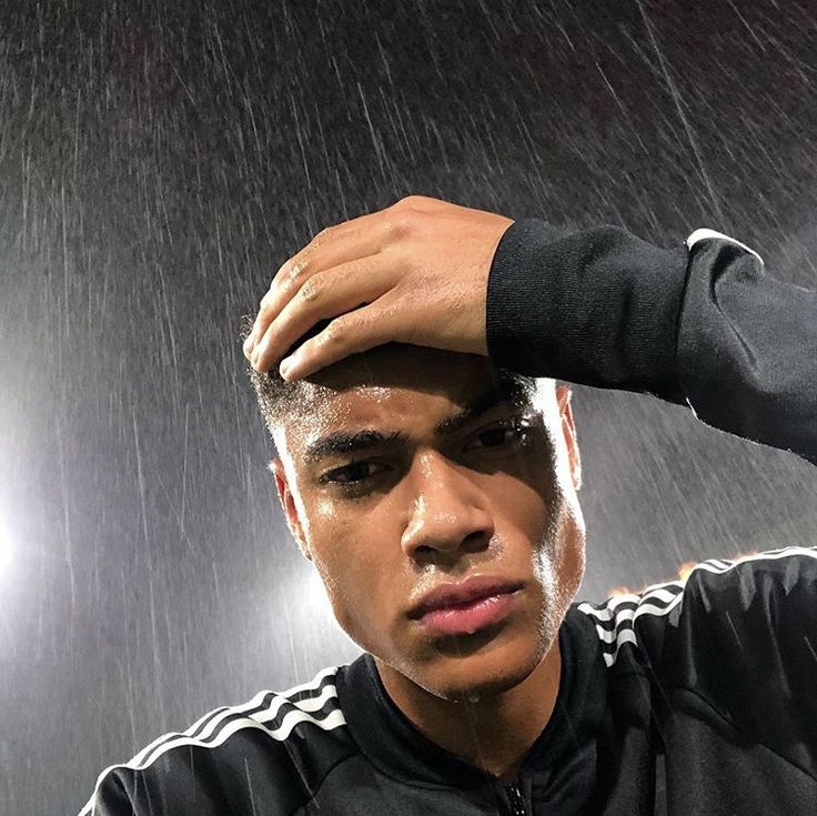 a young man holding his head in front of the camera while standing under a rain shower