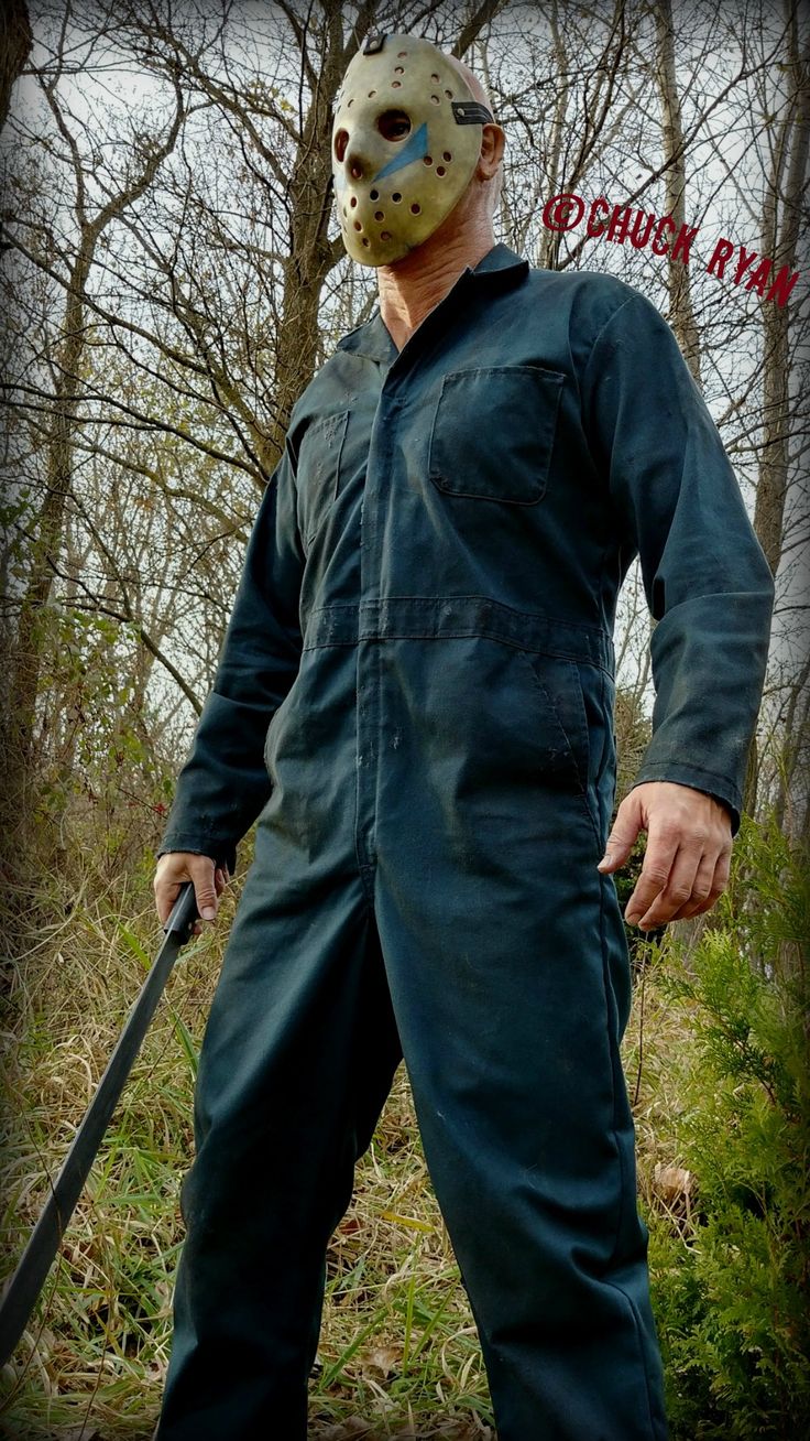 a man wearing a mask and holding a knife in his hand while walking through the woods