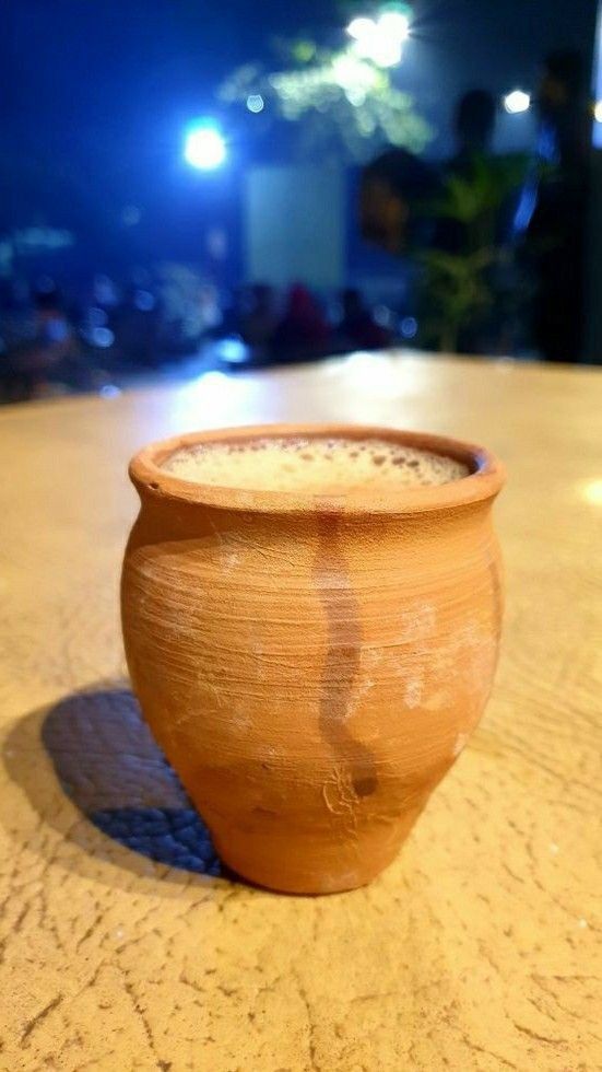 a brown pot sitting on top of a wooden table next to a cup filled with liquid