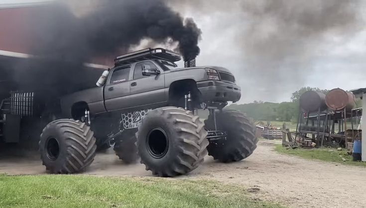 a monster truck with huge tires on it's back in front of a barn