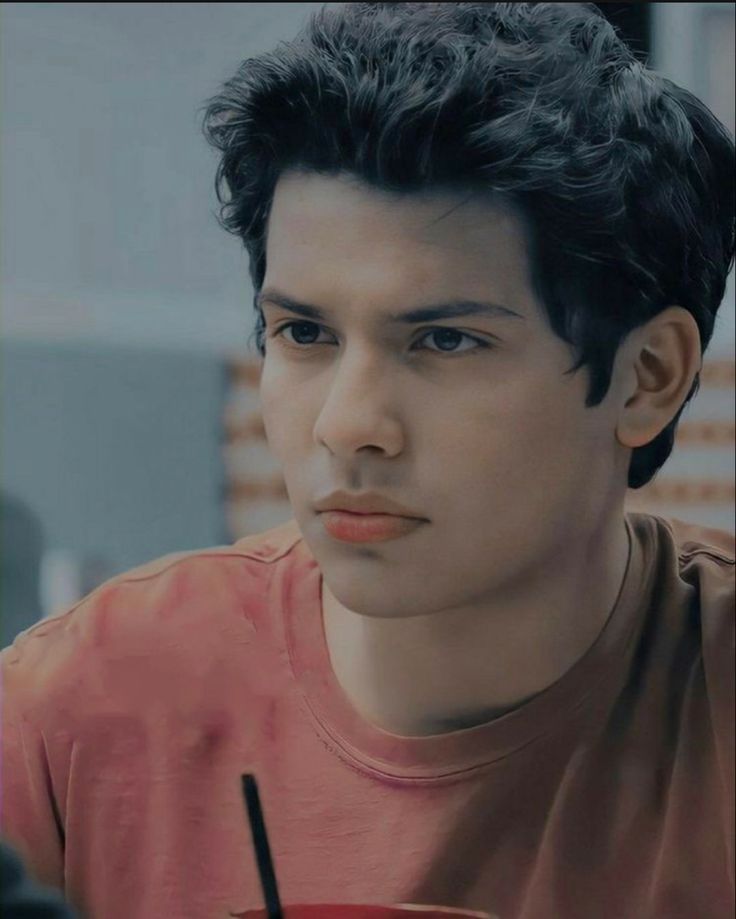 a young man sitting at a table with a drink in front of him and looking off to the side