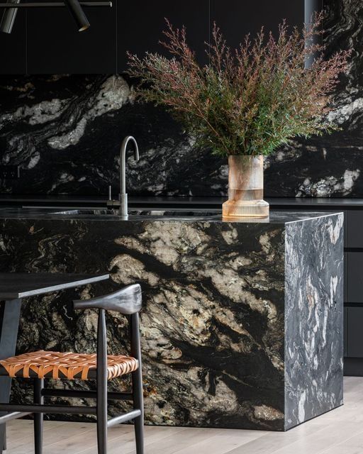 a kitchen with black marble counter tops and chairs in front of the sink, next to a potted plant