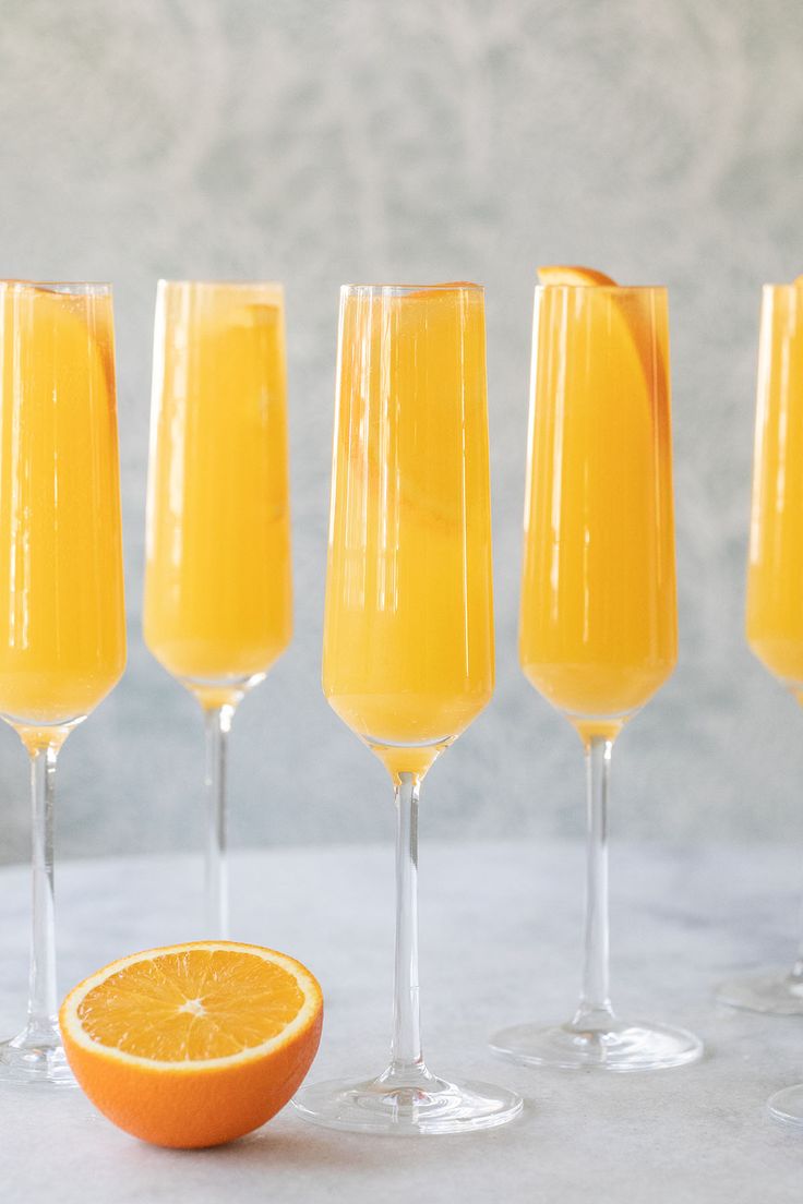 five glasses of orange juice next to an orange slice