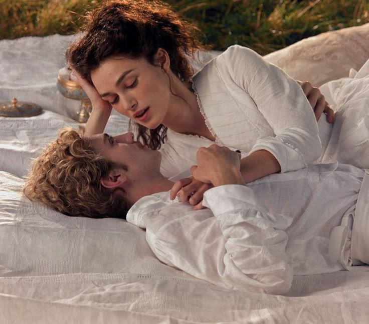 a man and woman laying on top of a bed next to each other in white clothes