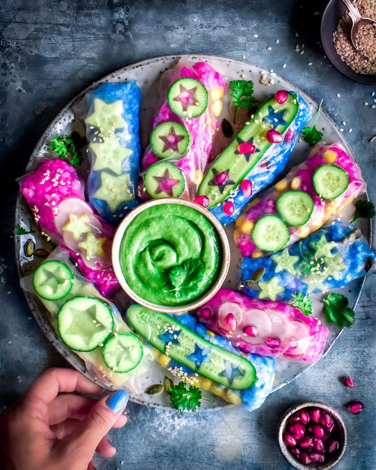 a plate filled with cucumbers and dips on top of a blue table