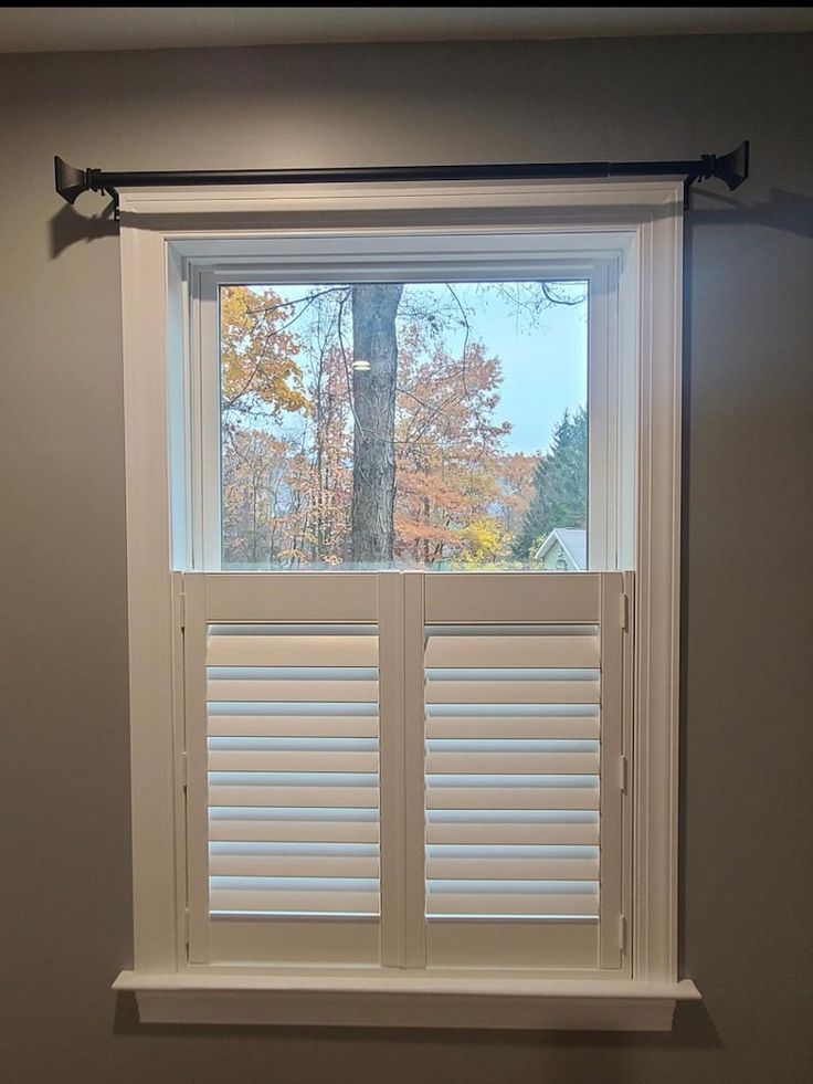 an empty room with white shutters on the window and a tree in the background