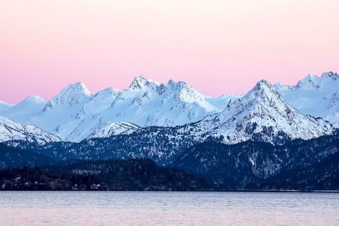 the mountains are covered in snow as the sun goes down over the water and it is pink