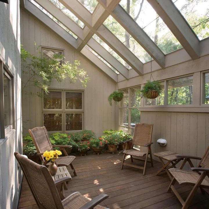 a wooden deck with chairs and potted plants on the top floor, under a glass roof