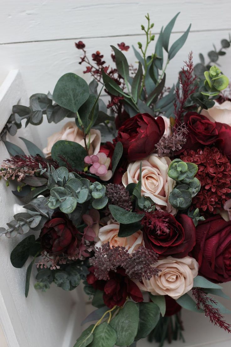 a bouquet of flowers sitting on top of a white bench with greenery and leaves