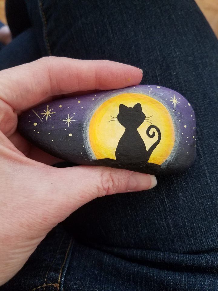 a person holding a painted rock with a cat on it