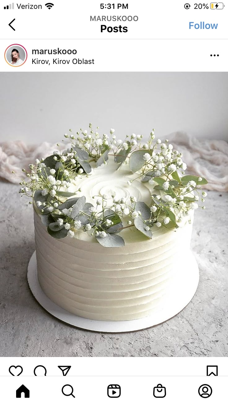 a white cake with flowers and greenery sitting on top of a table next to an instagram page